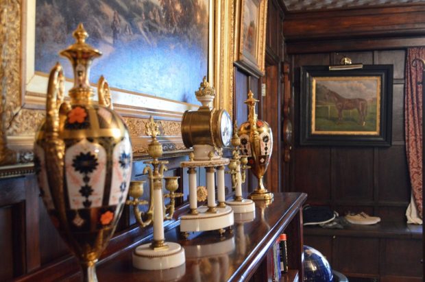 A wood panelled room with oil paintings on the walls and antiques on top of a wooden bookcase