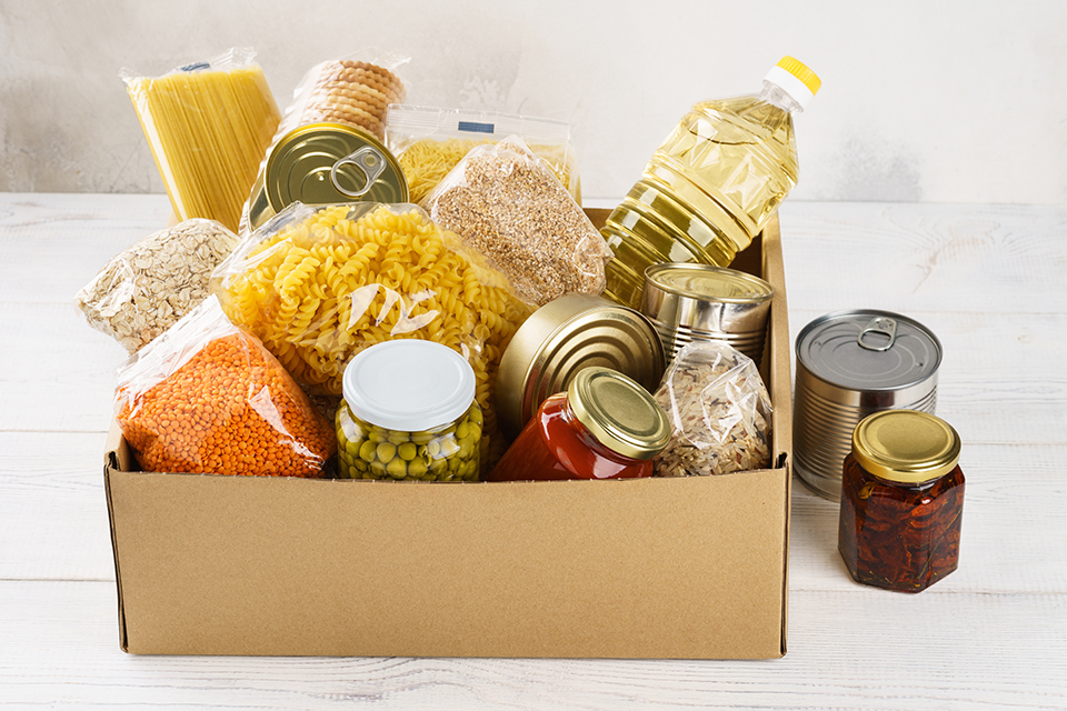 Various canned food, pasta and cereals in a cardboard box.