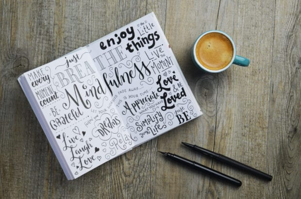 MINDFULNESS hand-lettered sketch notes in notepad on wooden desk with cup of coffee and pens