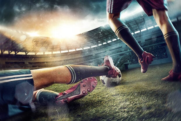 The legs of football players on green field of the stadium.