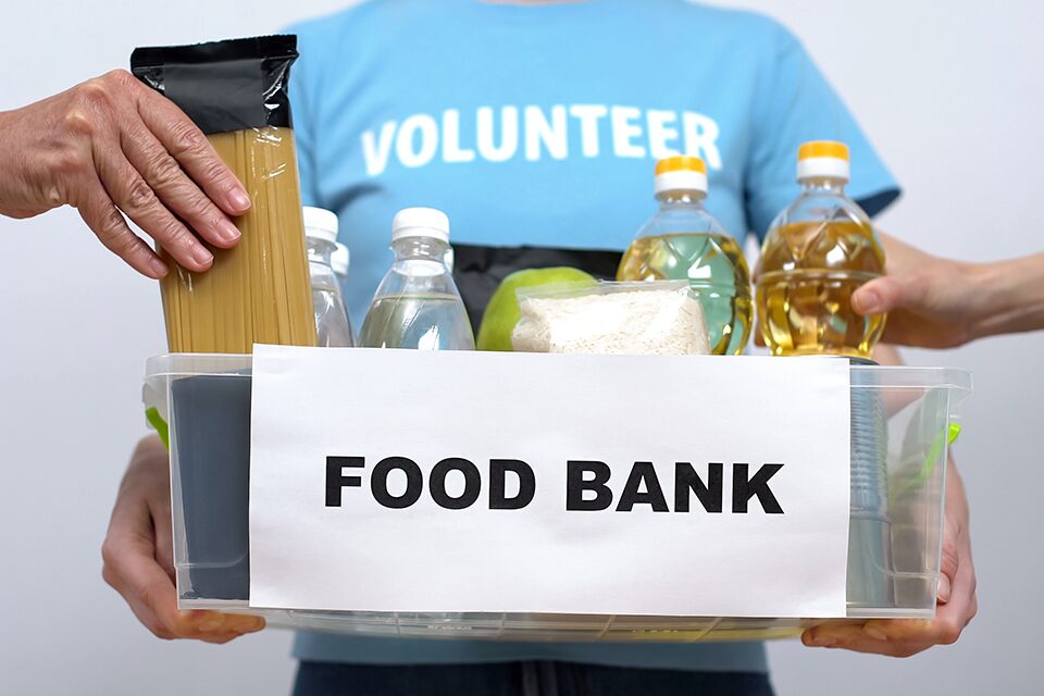 A foodbank volunteer holding a box of donations while other hands remove items from the box